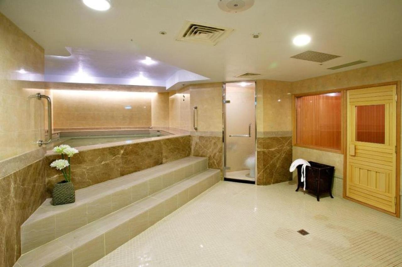 Evergreen Laurel Hotel - Taichung Exterior foto The photo shows a spacious and well-lit spa or wellness area. It features a large, recessed hot tub with steps leading up to it, surrounded by beige marble walls. There's a shower area enclosed in glass, and to the right, a wooden sauna or steam room