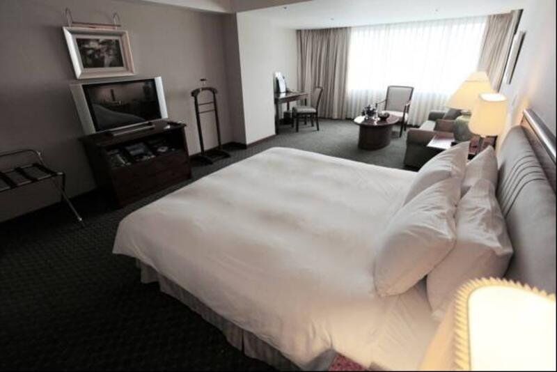 Evergreen Laurel Hotel - Taichung Exterior foto The photo shows a hotel room featuring a large bed with white bedding. There is a flat-screen television on a wooden cabinet opposite the bed. Nearby, there are two armchairs and a small table, creating a cozy seating area. Large windows allow natura