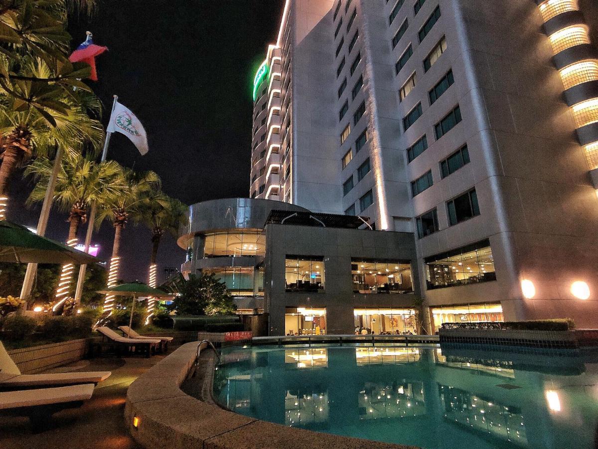 Evergreen Laurel Hotel - Taichung Exterior foto The photo depicts a modern hotel or building at night, featuring a sleek facade illuminated by lights. In the foreground, there is a swimming pool that reflects the surrounding lights and palm trees. There are lounge chairs near the pool, and the atm